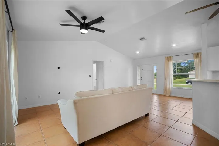 Living room with a ceiling fan, light tile patterned flooring, and vaulted ceiling