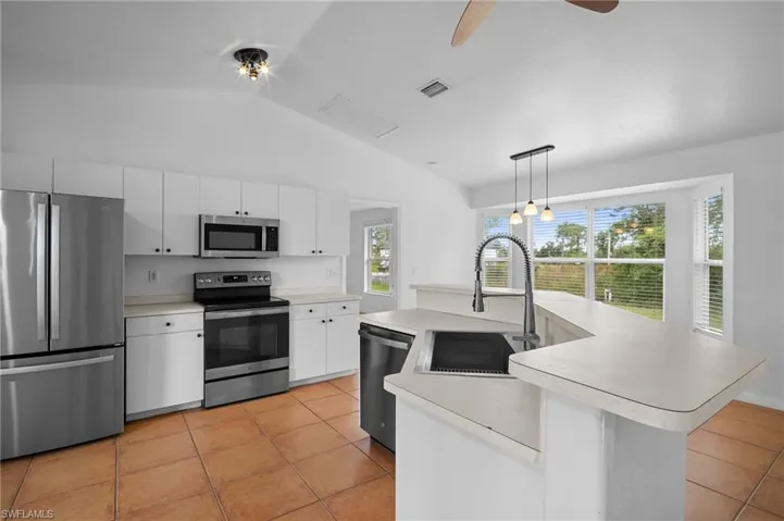 Kitchen with stainless steel appliances, light countertops, an island with sink, vaulted ceiling, and light tile patterned floors