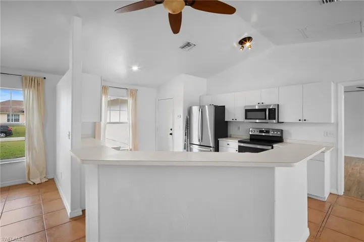 Kitchen with light tile patterned floors, light countertops, stainless steel appliances, white cabinets, and vaulted ceiling