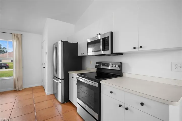 Kitchen featuring stainless steel electric stove, white cabinets, light countertops, and light tile patterned floors