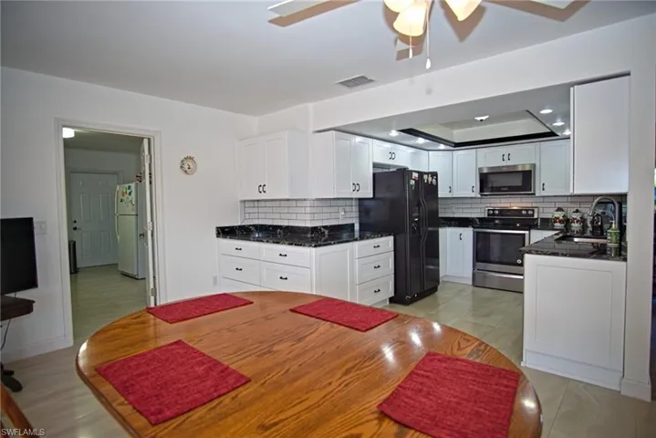 Kitchen with stainless steel appliances, white cabinetry, dark stone counters, ceiling fan, and a raised ceiling