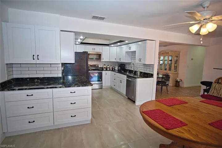 Kitchen with a ceiling fan, white cabinetry, stainless steel appliances, and dark stone countertops