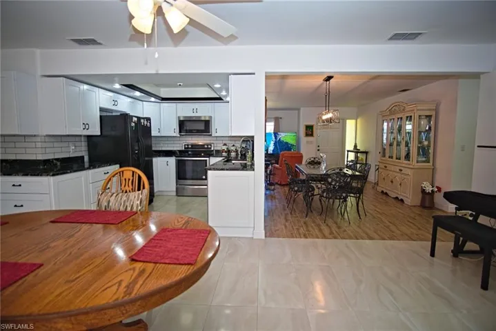 Kitchen with stainless steel appliances, ceiling fan, white cabinetry, dark stone counters, and backsplash