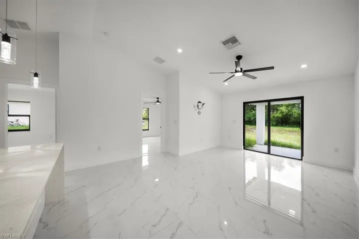 Empty room with ceiling fan, plenty of natural light, recessed lighting, light marble finish floors, and a high ceiling