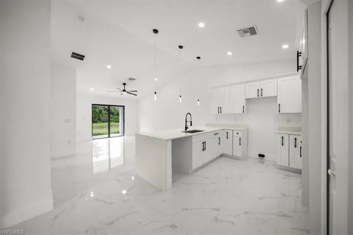 Kitchen featuring open floor plan, a peninsula, light marble finish flooring, recessed lighting, and lofted ceiling