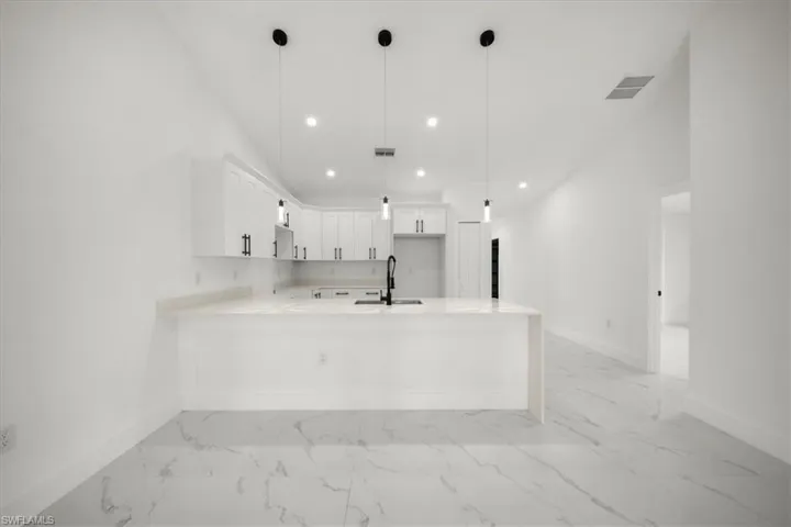 Kitchen featuring a peninsula, light countertops, recessed lighting, light marble finish flooring, and white cabinets