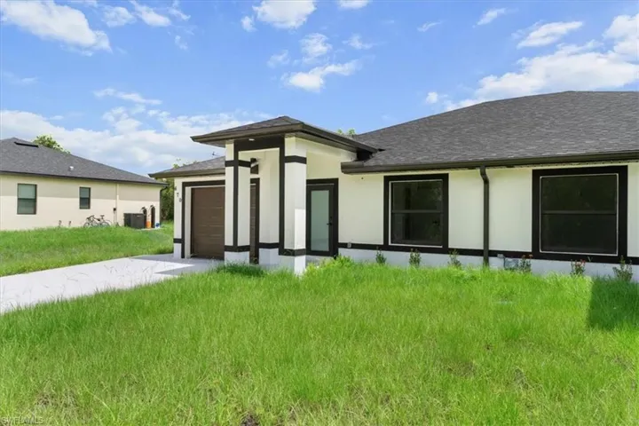 Rear view of property featuring a garage, roof with shingles, stucco siding, and driveway