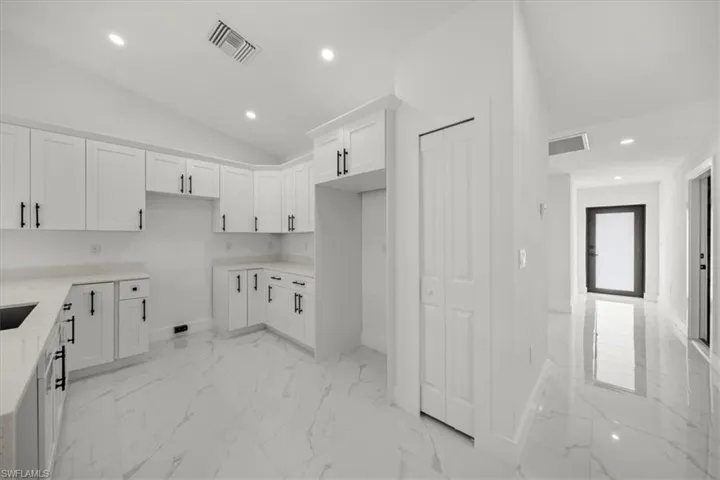 Kitchen featuring white cabinetry, light marble finish floors, vaulted ceiling, recessed lighting, and light countertops