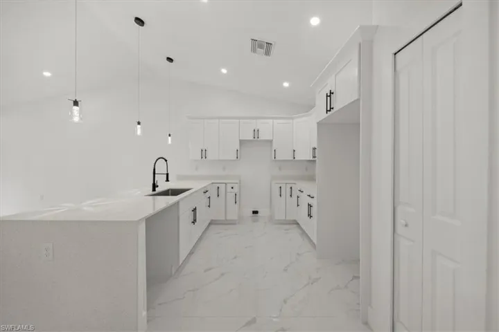 Kitchen with light marble finish flooring, recessed lighting, vaulted ceiling, white cabinets, and decorative light fixtures