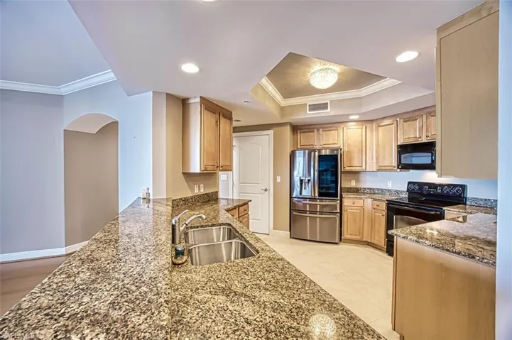 Kitchen with black appliances, dark stone countertops, a raised ceiling, and sink
