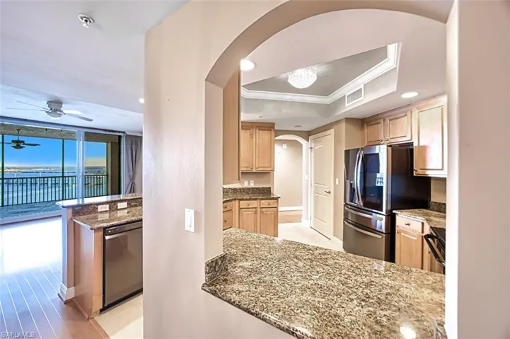 Kitchen with light stone countertops, light brown cabinetry, stainless steel appliances, a raised ceiling, and crown molding