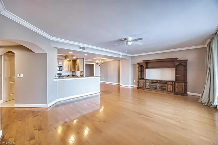 Unfurnished living room featuring ceiling fan with notable chandelier, crown molding, and light hardwood / wood-style flooring