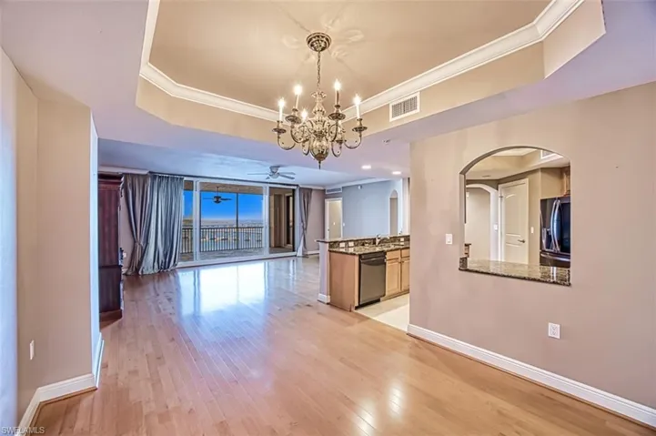 Kitchen featuring light wood-type flooring, dishwashing machine, ceiling fan with notable chandelier, a tray ceiling, and fridge with ice dispenser