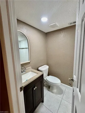 Half bath featuring a textured wall, vanity, a textured ceiling, and light tile patterned floors
