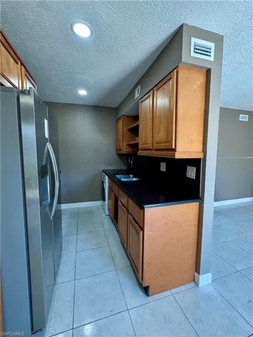 Kitchen with stainless steel fridge, a textured ceiling, wood finish cabinets, open shelves, and light tile patterned floors