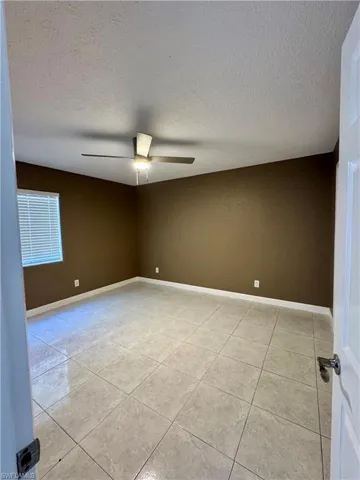 Unfurnished room featuring a textured ceiling, light tile patterned flooring, and ceiling fan