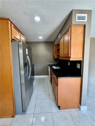Kitchen featuring a textured wall, wood finish cabinets, stainless steel fridge, a textured ceiling, and open shelves