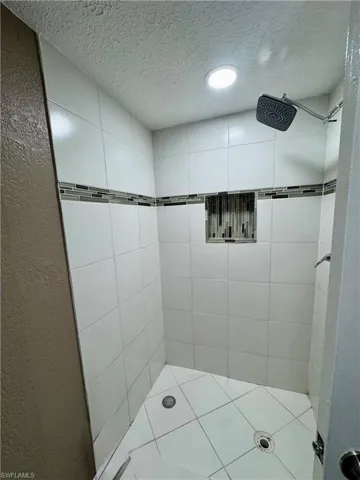 Full bath featuring a textured ceiling, a shower stall, and a textured wall