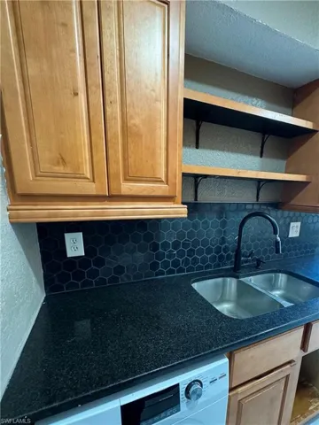 Kitchen with open shelves, backsplash, washer / dryer, dark stone counters, and light wood finish cabinets