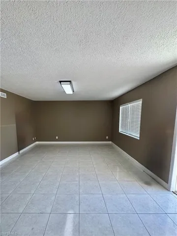 Empty room with a textured ceiling and light tile patterned flooring