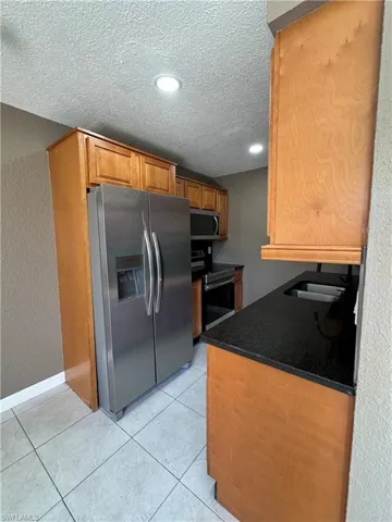 Kitchen with a textured wall, stainless steel appliances, a textured ceiling, light tile patterned floors, and wood finish cabinets