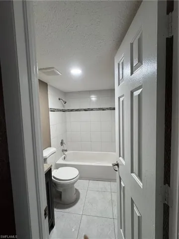 Bathroom featuring a textured ceiling, vanity, shower / bath combination, and light tile patterned floors