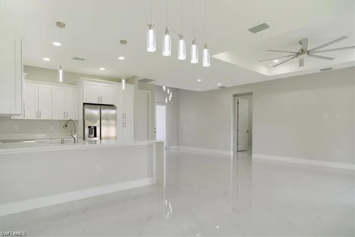 Kitchen featuring ceiling fan, hanging light fixtures, stainless steel fridge with ice dispenser, a center island with sink, and white cabinets