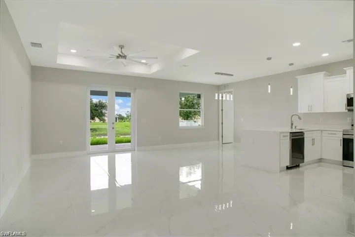 Unfurnished living room featuring ceiling fan, a raised ceiling, sink, and french doors
