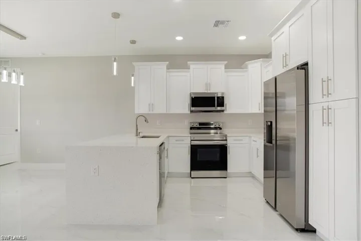 Kitchen with pendant lighting, stainless steel appliances, white cabinetry, and sink