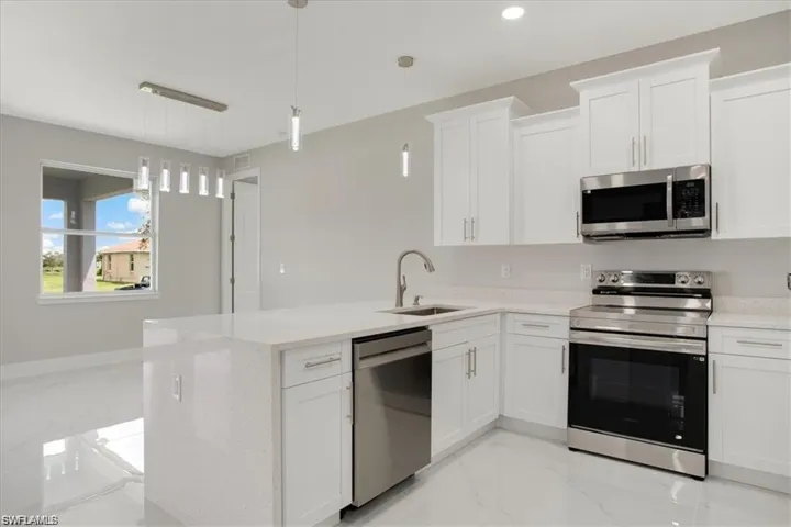 Kitchen featuring white cabinets, decorative light fixtures, sink, and appliances with stainless steel finishes