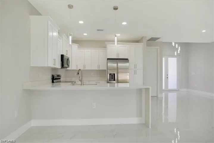 Kitchen with sink, stainless steel appliances, kitchen peninsula, decorative light fixtures, and white cabinets