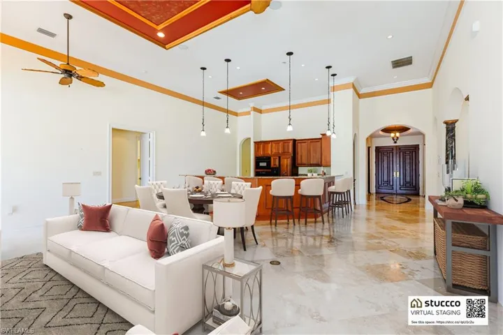 Living room with a high ceiling, crown molding, ceiling fan, and light tile floors