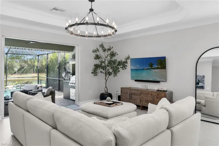 Living room featuring a sunroom, ornamental molding, a raised ceiling, and hanging lights