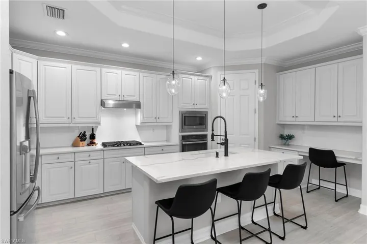 Kitchen featuring a kitchen bar, white cabinetry, stainless steel appliances, crown molding, and light wood-type flooring