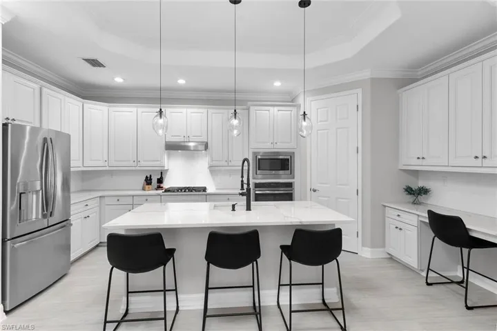 Kitchen featuring stainless steel appliances, white cabinetry, a breakfast bar area, crown molding, and a tray ceiling