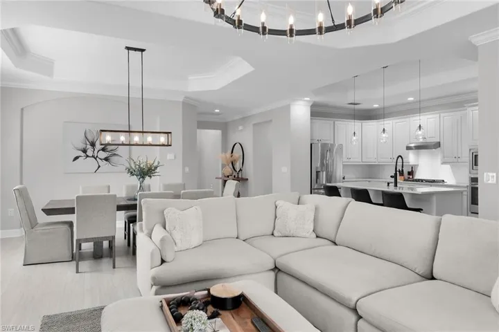 Living room featuring a tray ceiling, crown molding, suspended lighting, and light wood finished floors