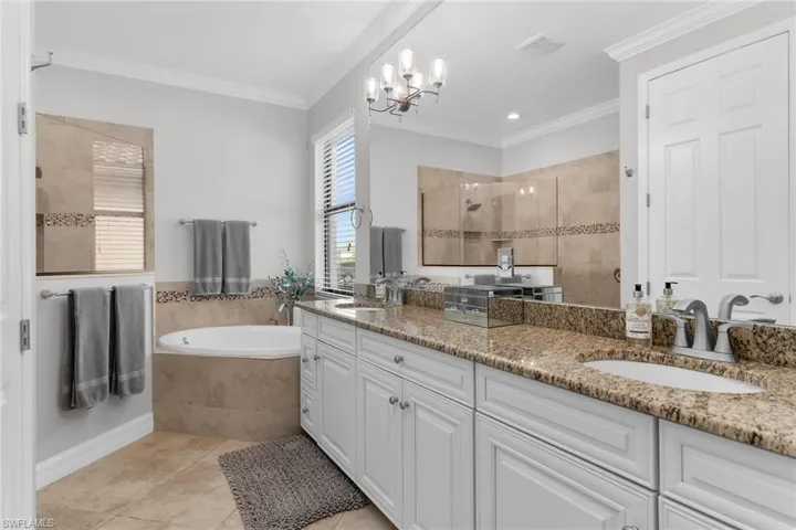 Bathroom featuring walk in shower, double vanity, ornamental molding, a bath, and suspended lighting