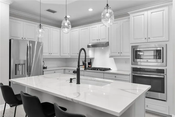 Kitchen featuring stainless steel appliances, an island with sink, light stone countertops, a breakfast bar area, and white cabinetry
