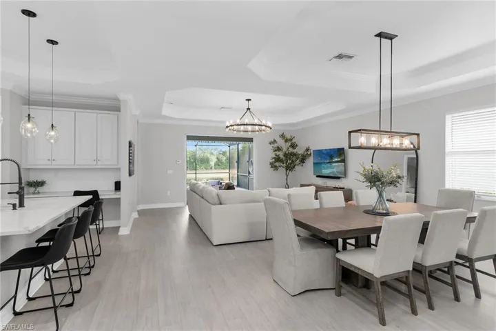 Dining room with a tray ceiling, hanging lights, light wood finished floors, and crown molding