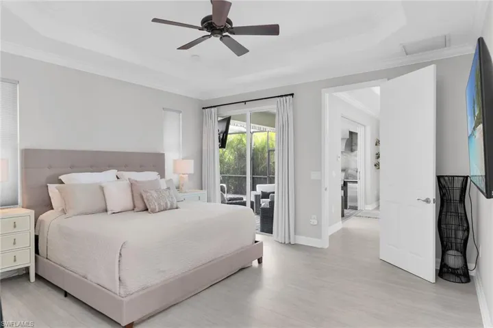 Bedroom with access to outside, a raised ceiling, ceiling fan, crown molding, and light wood-type flooring