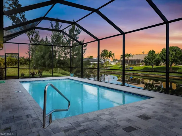 Pool at dusk featuring a water view, a patio area, and a lanai