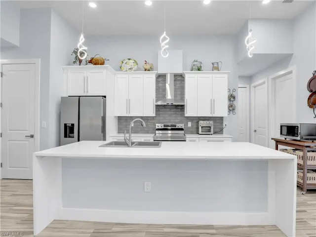 Kitchen with wall chimney exhaust hood, sink, stainless steel appliances, hanging light fixtures, and white cabinets