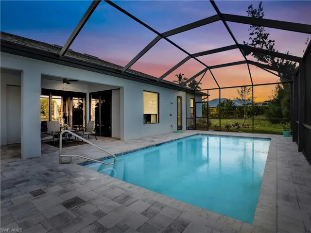 Pool at dusk featuring a lanai, ceiling fan, and a patio