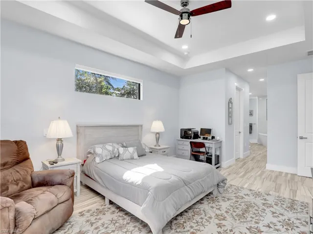 Bedroom with ceiling fan, a tray ceiling, and light hardwood / wood-style floors