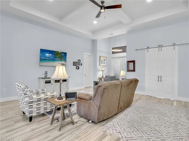 Living room featuring ceiling fan, beam ceiling, light wood-type flooring, a towering ceiling, and a barn door