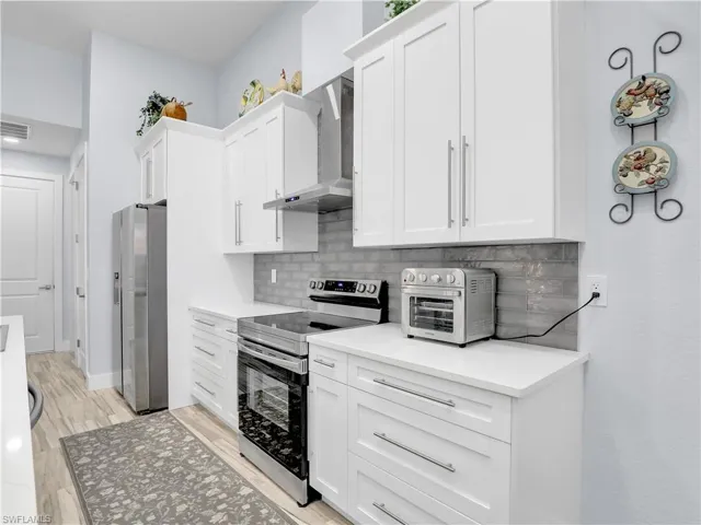 Kitchen with wall chimney range hood, white cabinetry, light hardwood / wood-style flooring, appliances with stainless steel finishes, and backsplash