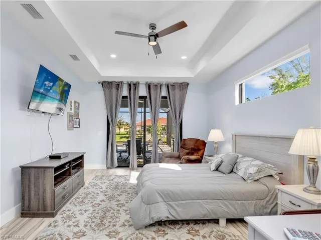 Bedroom featuring access to outside, a tray ceiling, light hardwood / wood-style flooring, and ceiling fan