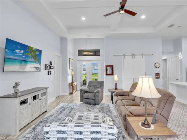 Living room with ceiling fan, a barn door, a tray ceiling, and light hardwood / wood-style floors
