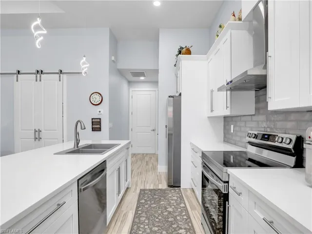 Kitchen with stainless steel appliances, white cabinets, sink, a barn door, and decorative light fixtures
