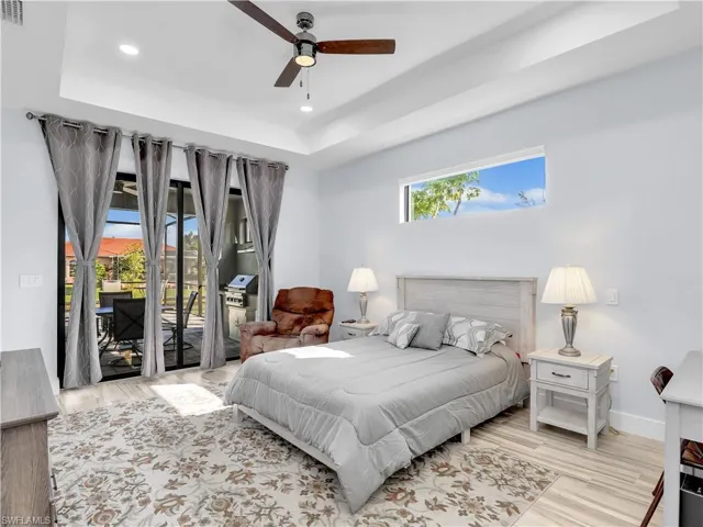Bedroom with a raised ceiling, access to outside, light hardwood / wood-style floors, and ceiling fan
